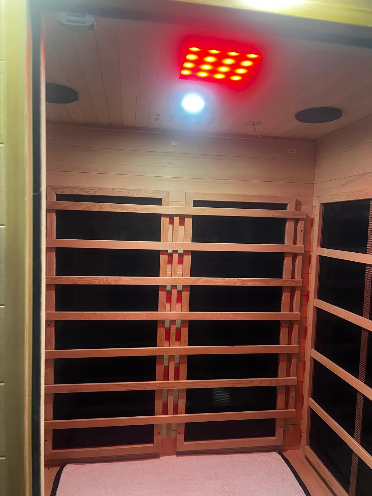 Wooden sauna interior with heater panels and coloured ceiling lighting